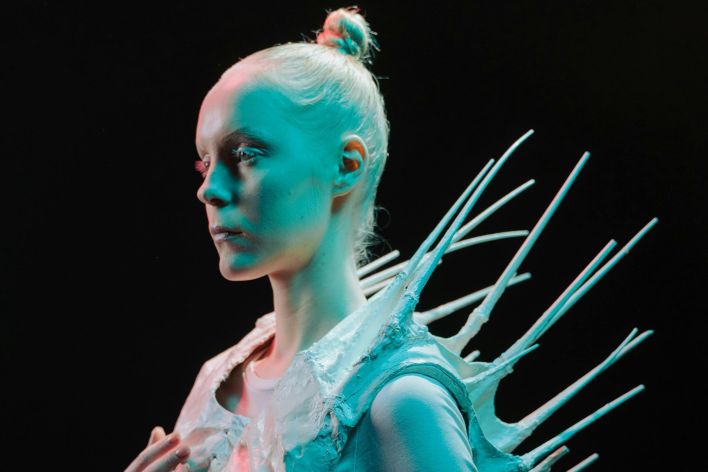 A woman in a spiky sci-fi costume under dramatic lighting on a black background.