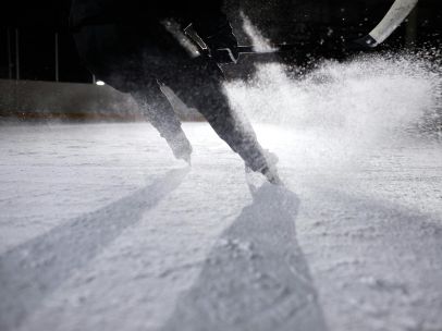 High-energy ice hockey player in action, creating an ice spray during a game on a frozen rink.