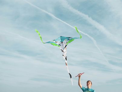 A young man in a blue shirt flying a colorful kite in a clear sky, enjoying the breeze.