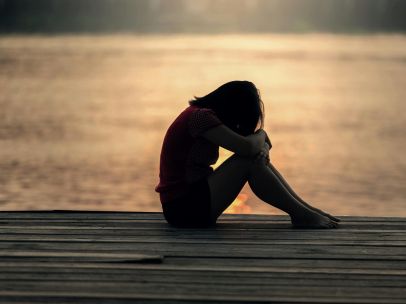 A woman sitting alone on a wooden dock by the lake, showing solitude and reflection.