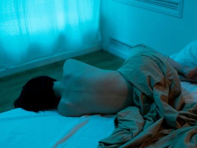 A person lies on a bed in a dimly lit, moody room, evoking solitude and tranquility.