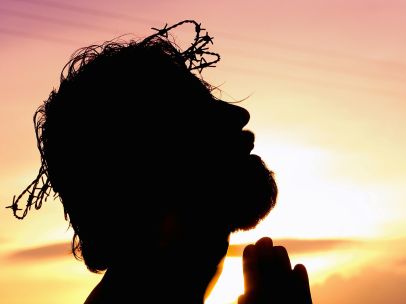 A silhouette of a man praying at sunset, wearing a crown of thorns, symbolizing faith and hope.