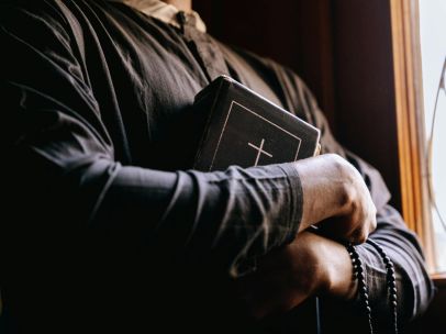 A priest holding a Bible by a sunlit window, symbolizing faith and spirituality.