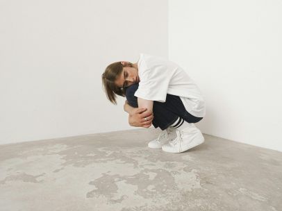 Person crouched in a white corner reflects solitude or contemplation.